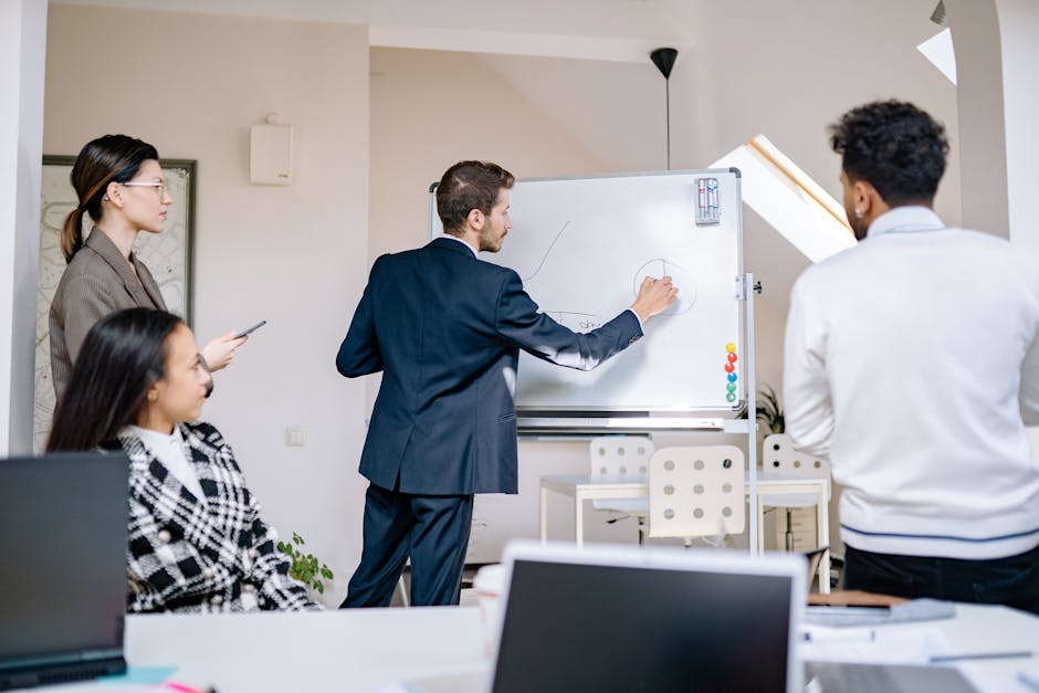 Group of business professionals engaged in a collaborative meeting with whiteboard discussions in a modern office.